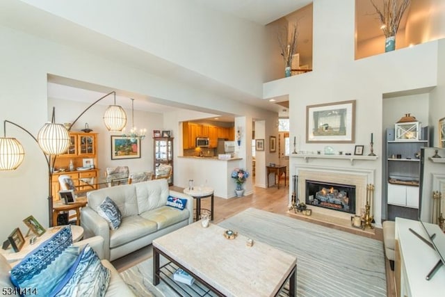 living room featuring light wood-type flooring, a warm lit fireplace, and a chandelier