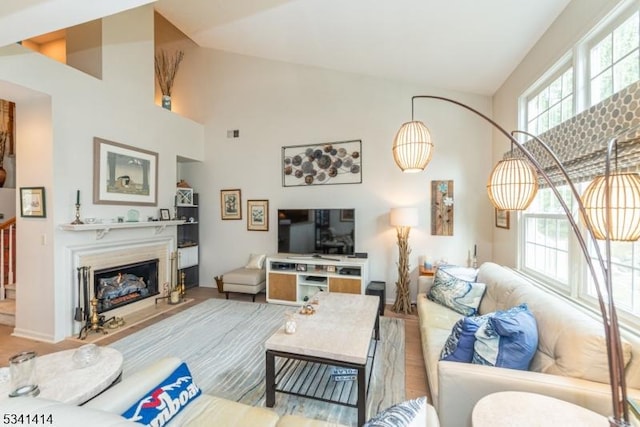 living area with visible vents, wood finished floors, high vaulted ceiling, and a glass covered fireplace