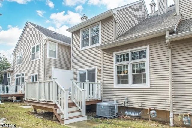 back of house featuring roof with shingles, a wooden deck, a yard, central AC, and a chimney