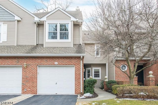 view of property with driveway, a chimney, a shingled roof, a garage, and brick siding