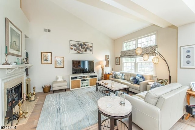 living area featuring visible vents, wood finished floors, high vaulted ceiling, and a fireplace with raised hearth