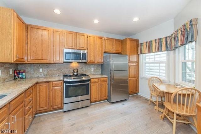 kitchen featuring light stone counters, backsplash, stainless steel appliances, and light wood-style floors