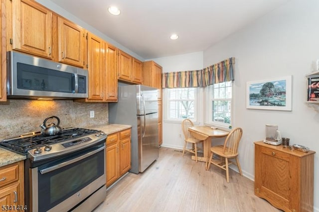 kitchen with light wood-style flooring, light stone counters, tasteful backsplash, stainless steel appliances, and baseboards