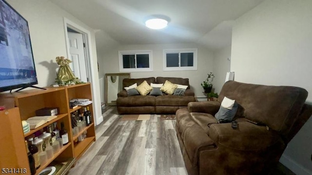 living area with vaulted ceiling, baseboards, and wood finished floors