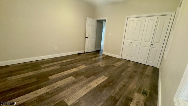 unfurnished bedroom with dark wood-style floors, visible vents, baseboards, and a closet