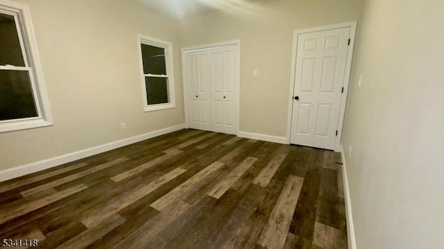 unfurnished bedroom with dark wood-type flooring, a closet, and baseboards