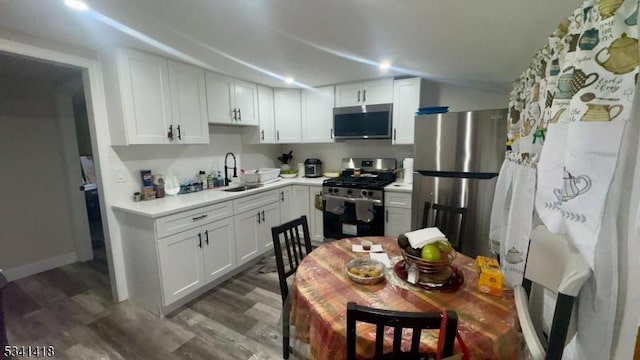 kitchen featuring wood finished floors, a sink, white cabinetry, light countertops, and appliances with stainless steel finishes