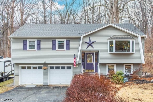 bi-level home with roof with shingles, driveway, a chimney, and an attached garage