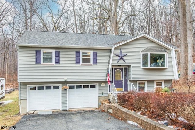 bi-level home featuring aphalt driveway, an attached garage, and a shingled roof