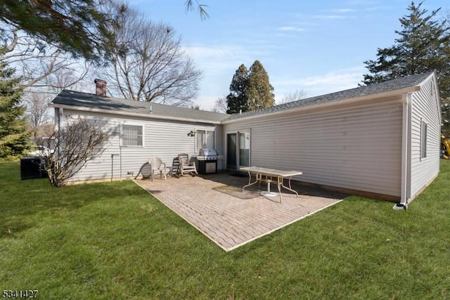 rear view of house with a chimney, a patio, and a yard