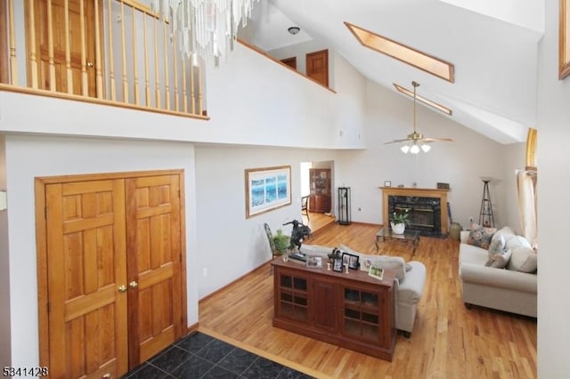 living room featuring a skylight, a glass covered fireplace, ceiling fan, wood finished floors, and high vaulted ceiling