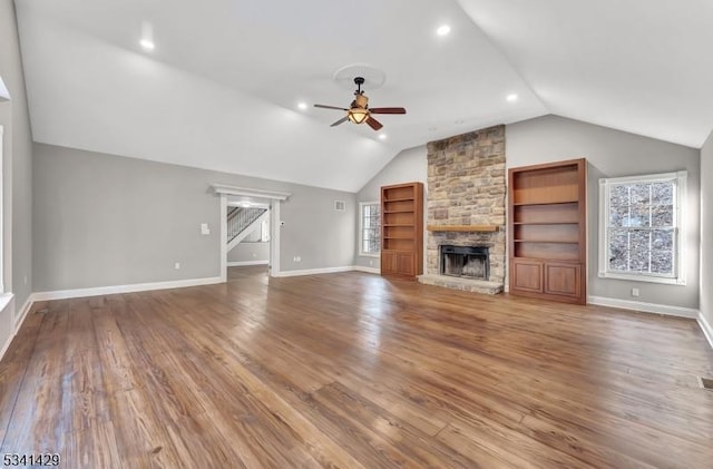 unfurnished living room with vaulted ceiling, a stone fireplace, wood finished floors, and a ceiling fan