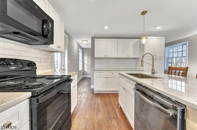 kitchen with light wood finished floors, light stone countertops, black appliances, white cabinetry, and a sink