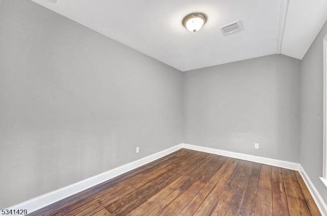 spare room featuring dark wood-style floors, visible vents, baseboards, and vaulted ceiling