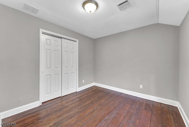 unfurnished bedroom with visible vents, baseboards, vaulted ceiling, a closet, and dark wood-style floors