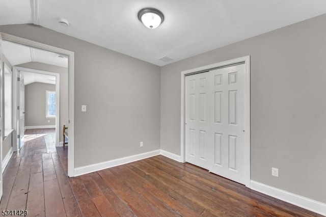 unfurnished bedroom with lofted ceiling, baseboards, and dark wood-style flooring