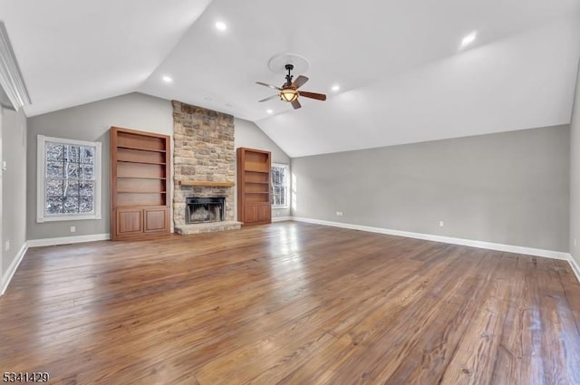 unfurnished living room with baseboards, lofted ceiling, ceiling fan, hardwood / wood-style floors, and a stone fireplace