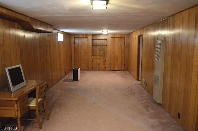 below grade area with a heating unit, light colored carpet, and wooden walls