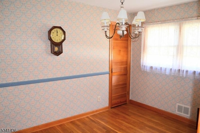 empty room with visible vents, an inviting chandelier, wood finished floors, baseboards, and wallpapered walls