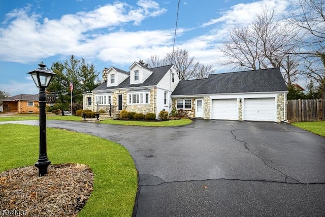 new england style home with a garage, fence, driveway, stone siding, and a front yard