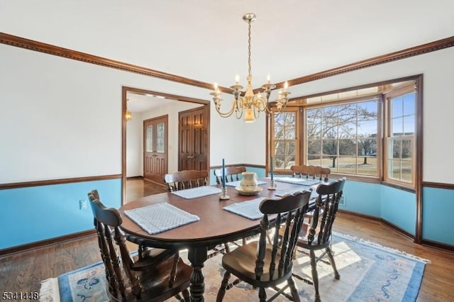 dining room with a notable chandelier, baseboards, wood finished floors, and ornamental molding