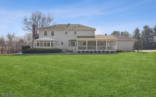 rear view of property with a sunroom, a yard, and a chimney