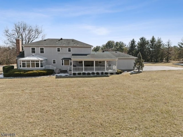 rear view of house with a sunroom, a chimney, and a yard