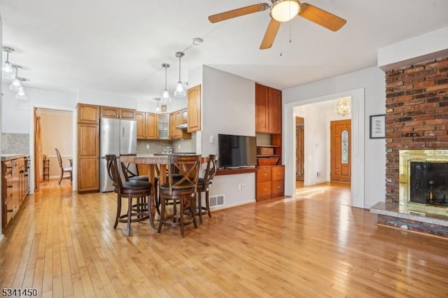 dining room featuring a brick fireplace, visible vents, light wood finished floors, and ceiling fan