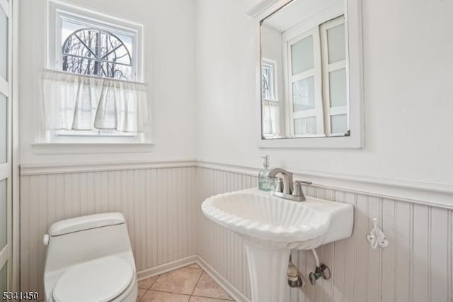 bathroom featuring tile patterned floors, a wainscoted wall, toilet, and a sink