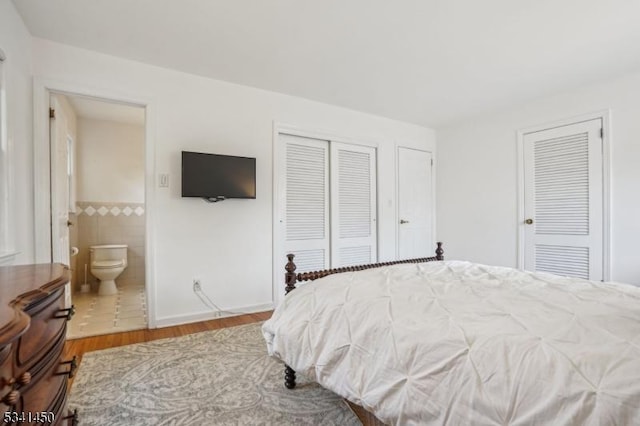 bedroom featuring wood finished floors, a wainscoted wall, tile walls, two closets, and connected bathroom