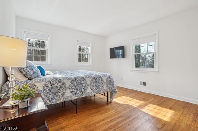 bedroom with visible vents, multiple windows, baseboards, and wood-type flooring