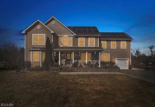 rear view of house featuring aphalt driveway, a porch, a lawn, an attached garage, and roof mounted solar panels