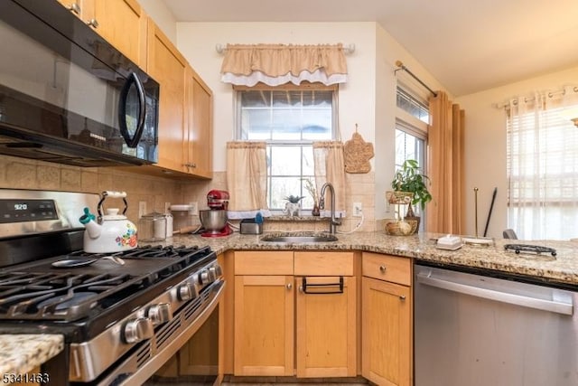 kitchen featuring light stone countertops, tasteful backsplash, appliances with stainless steel finishes, and a sink