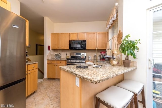 kitchen with a peninsula, a sink, stainless steel appliances, a kitchen breakfast bar, and backsplash