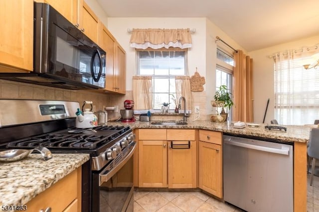 kitchen with a sink, light stone countertops, appliances with stainless steel finishes, and a peninsula