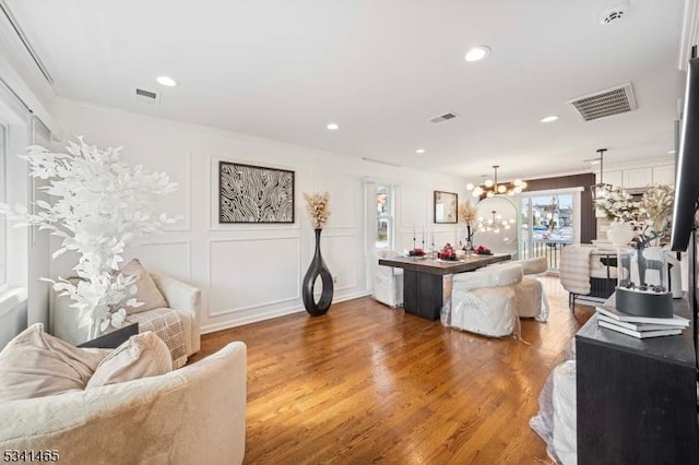 living area featuring a chandelier, a decorative wall, wood finished floors, visible vents, and crown molding