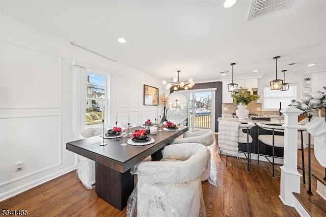 dining space with dark wood-style flooring, crown molding, a notable chandelier, visible vents, and a decorative wall