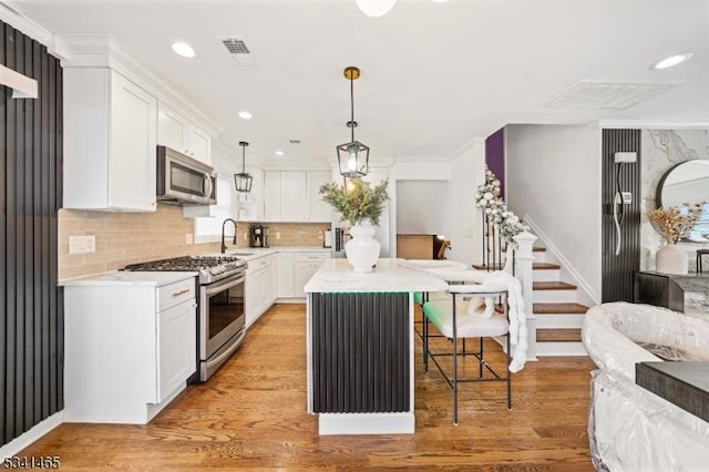 kitchen with light wood-style flooring, a kitchen island, appliances with stainless steel finishes, light countertops, and white cabinetry