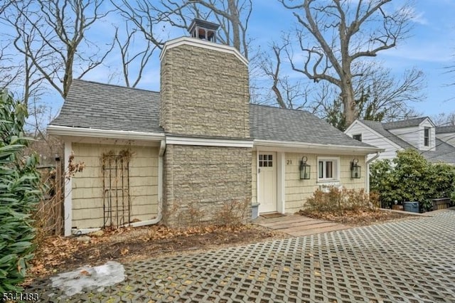 exterior space featuring stone siding, roof with shingles, and a chimney