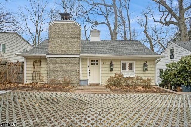 view of front of house featuring a shingled roof, stone siding, fence, and a chimney