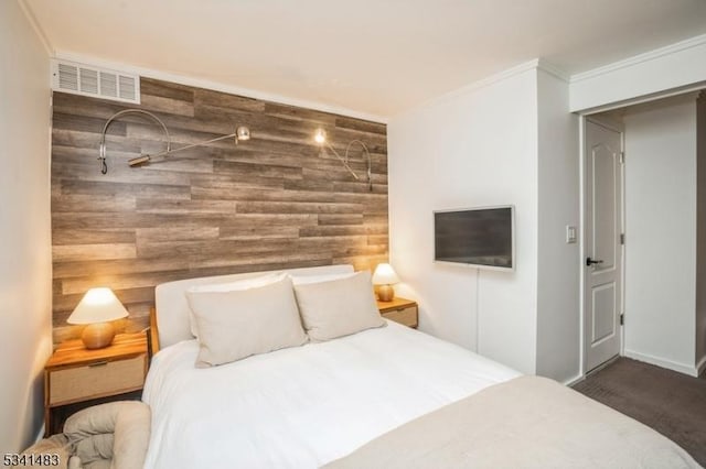 bedroom with an accent wall, wood walls, carpet flooring, visible vents, and ornamental molding