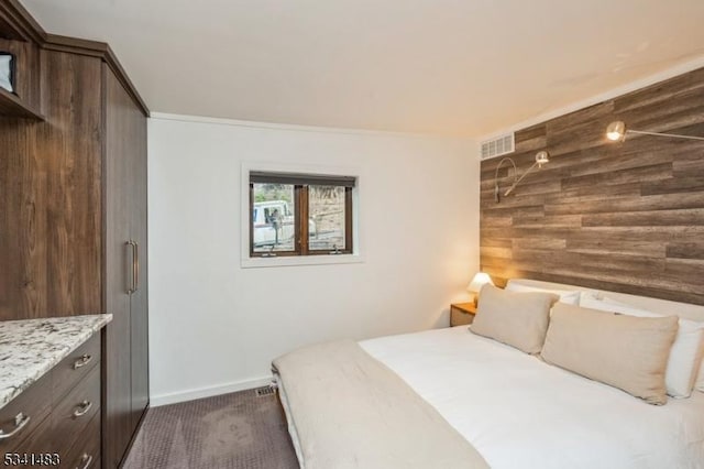 bedroom with an accent wall, wood walls, visible vents, baseboards, and dark carpet