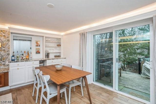 dining area with light wood-style floors, bar area, and crown molding