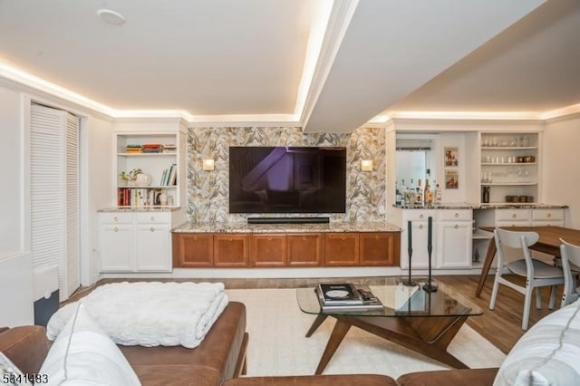 living room with built in features, a tray ceiling, and ornamental molding