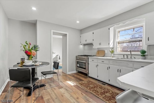 kitchen featuring a sink, white cabinets, light wood-style floors, light countertops, and high end range