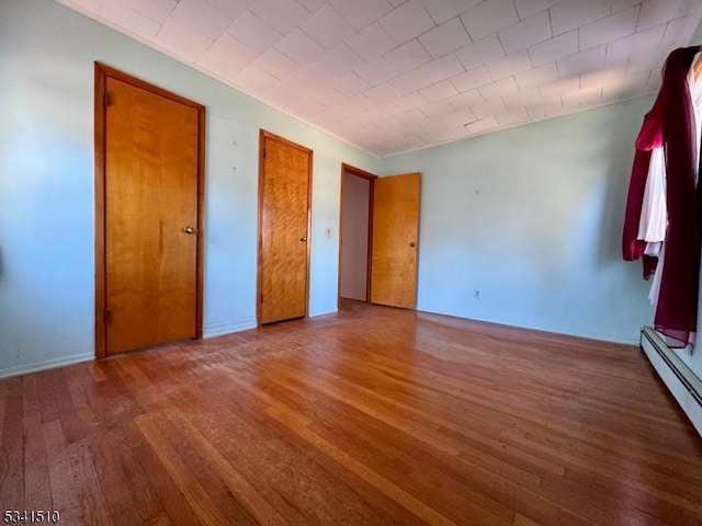 unfurnished bedroom featuring baseboard heating and wood finished floors