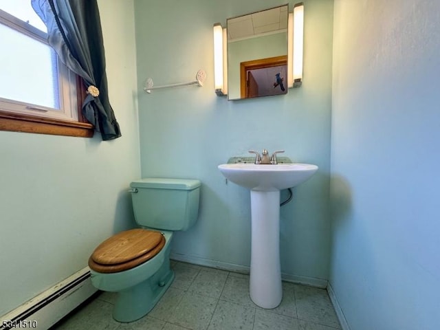 half bathroom with a baseboard radiator, toilet, a sink, baseboards, and tile patterned floors