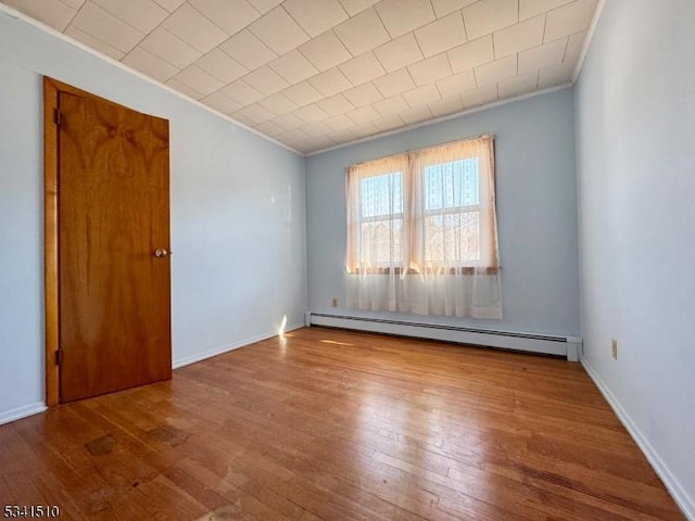 spare room featuring baseboard heating, wood-type flooring, and baseboards