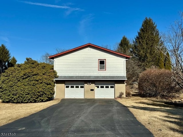 view of side of home featuring aphalt driveway, an attached garage, a shingled roof, and stucco siding