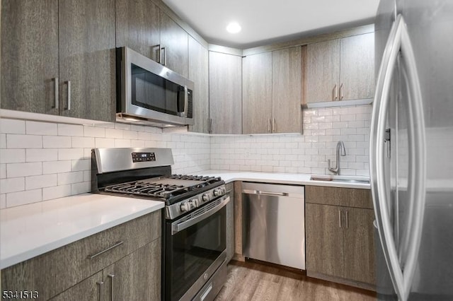 kitchen featuring light wood finished floors, a sink, appliances with stainless steel finishes, light countertops, and decorative backsplash